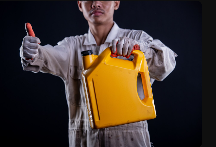 Hombre moreno con mameluco blanco y guantes de seguridad sosteniendo con la mano izquierda una galonera de l&iacute;quido de frenos.