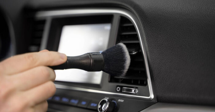 persona haciendo una limpieza superficial de las ventanillas del aire acondicionado de su auto